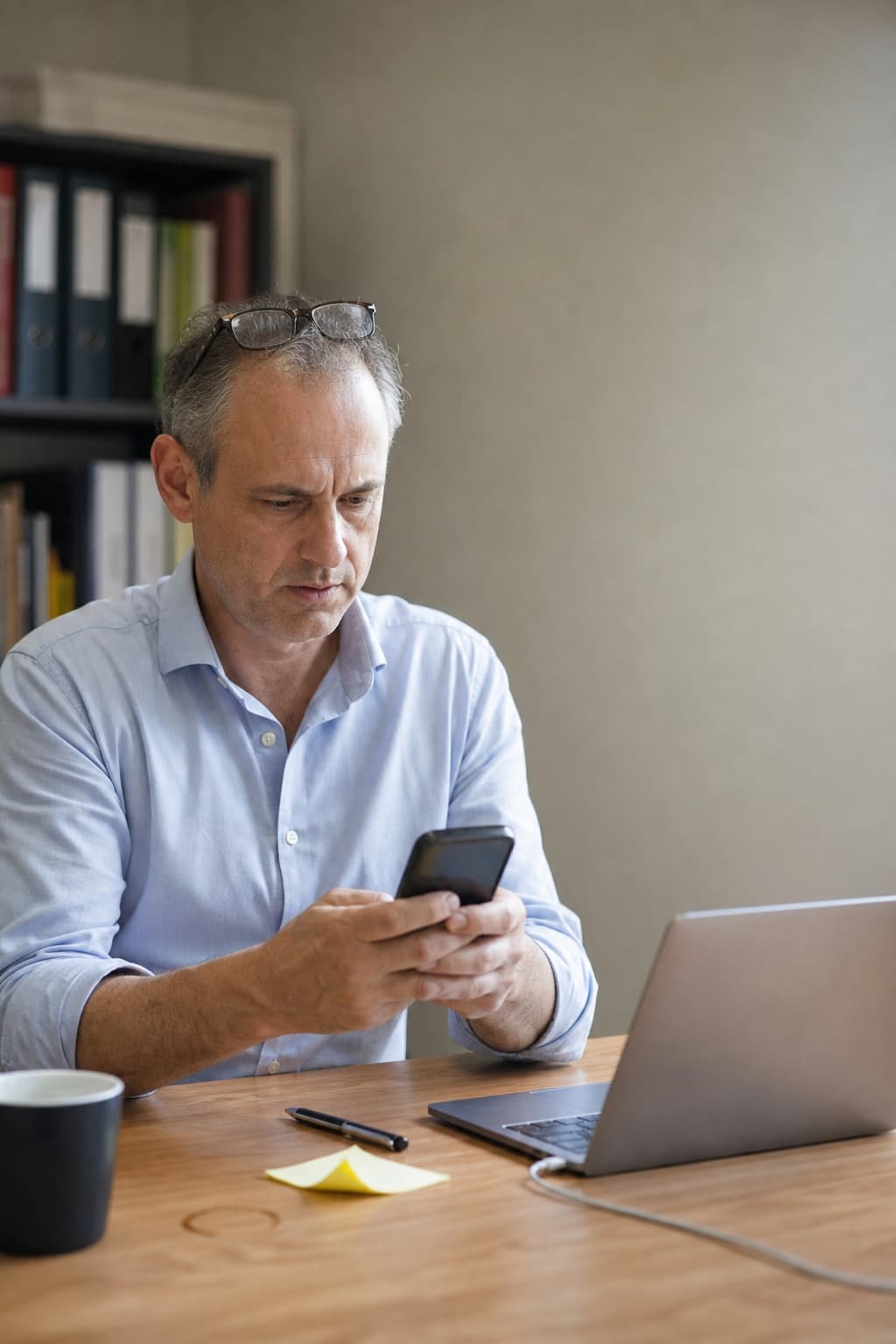 A principal in his own office reading his firm's listing on his phone, recognising something out of date.