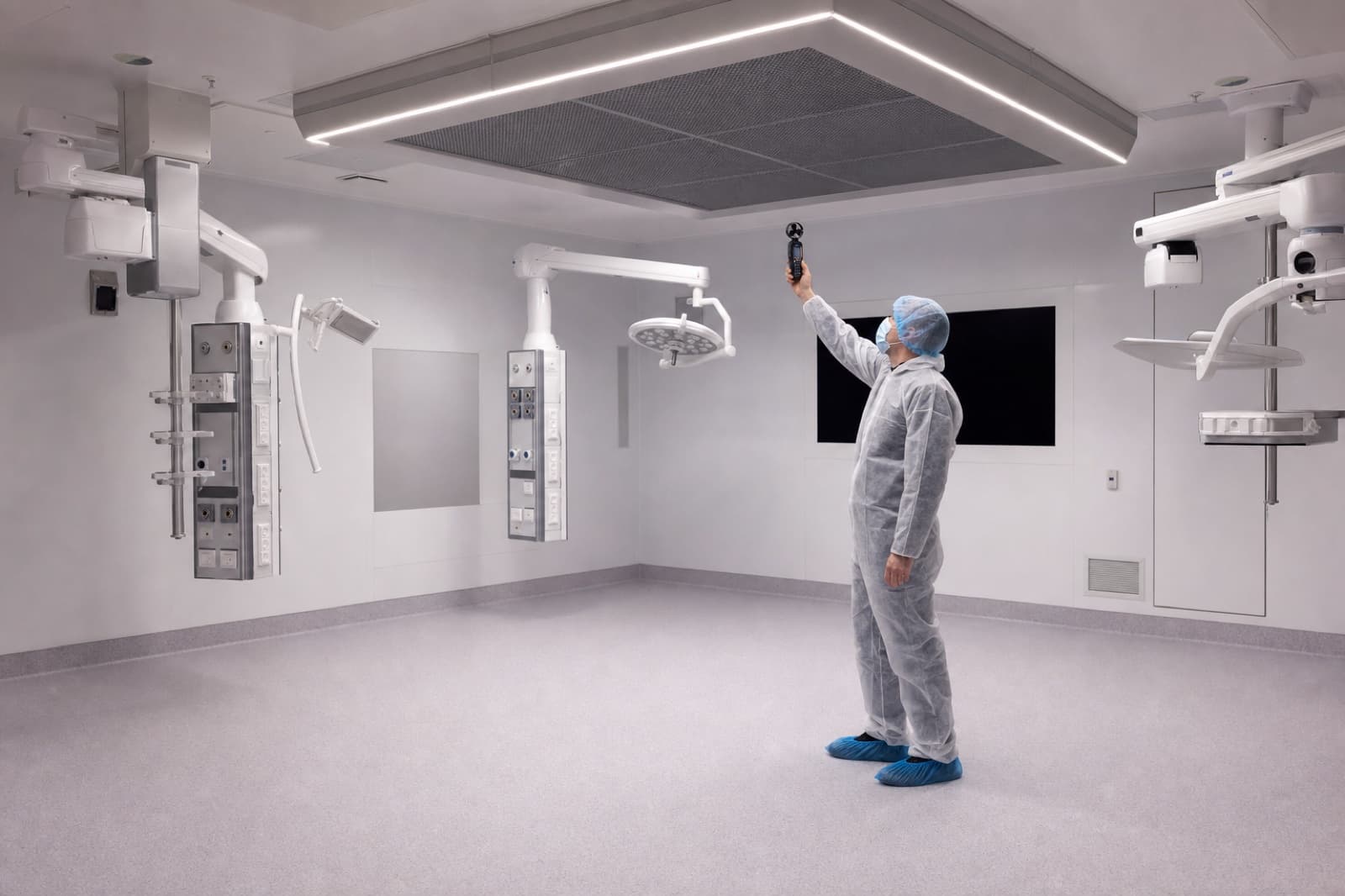 Commissioning engineer taking an air velocity reading beneath a laminar flow canopy in an operating theatre