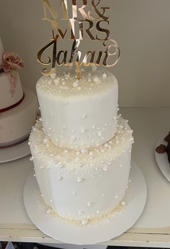 Two-tier ivory wedding cake with pearl detailing and a 'Mr & Mrs Jahan' gold topper