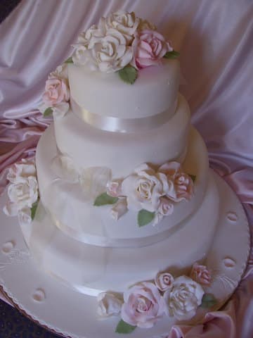 Three-tier white wedding cake with cascading sugar roses on pink fabric