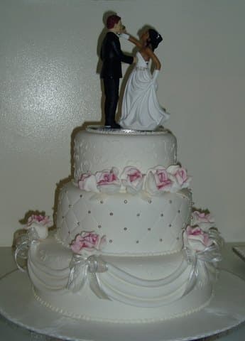 Three-tier classic white wedding cake with pink sugar roses and bride-and-groom topper