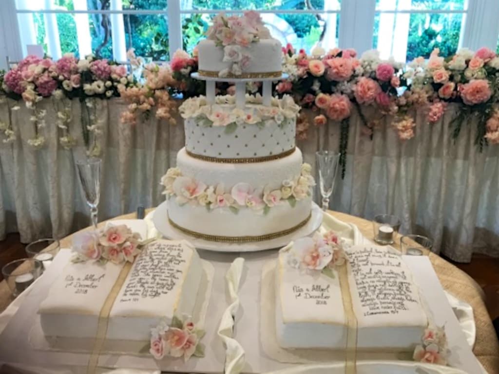 Tall pillar-separated wedding cake at a reception venue with floral arrangements and matching sheet cakes