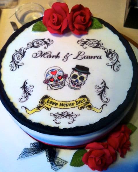 Day-of-the-Dead themed wedding cake with hand-painted sugar skulls reading 'Mark & Laura — Love Never Dies'