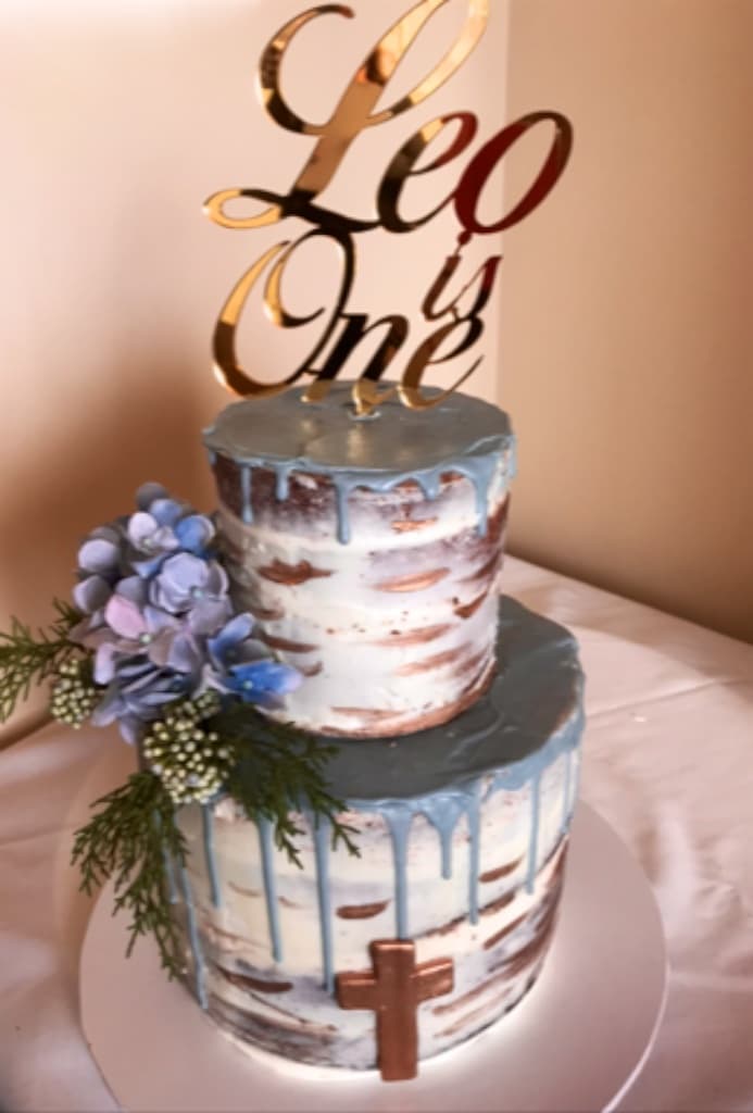 Two-tier semi-naked drip cake in blue and copper with hydrangeas and a 'Leo is One' gold topper